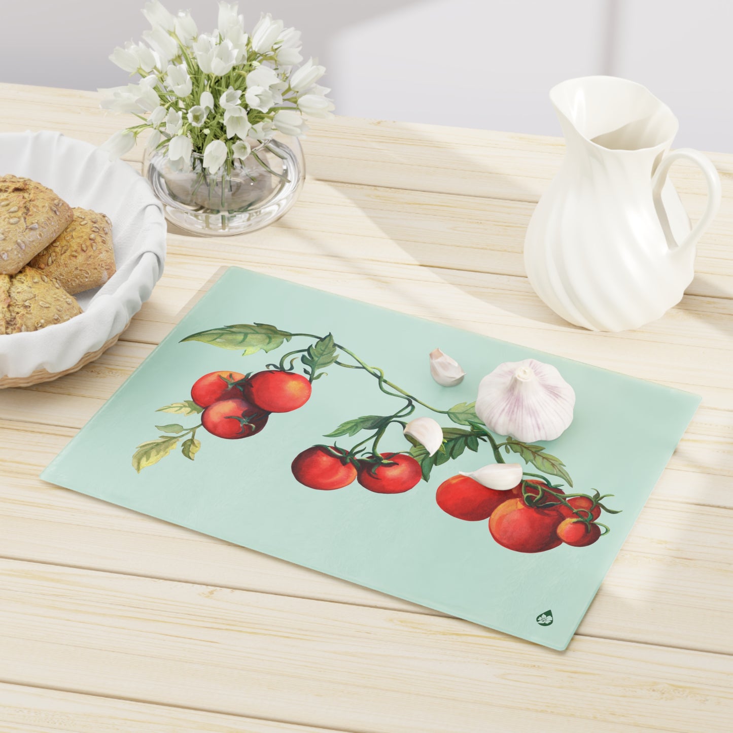 Flat view of Large Jersey Fresh Tomato tempered glass cutting board on table with pitcher vase of flowers and basket of bread