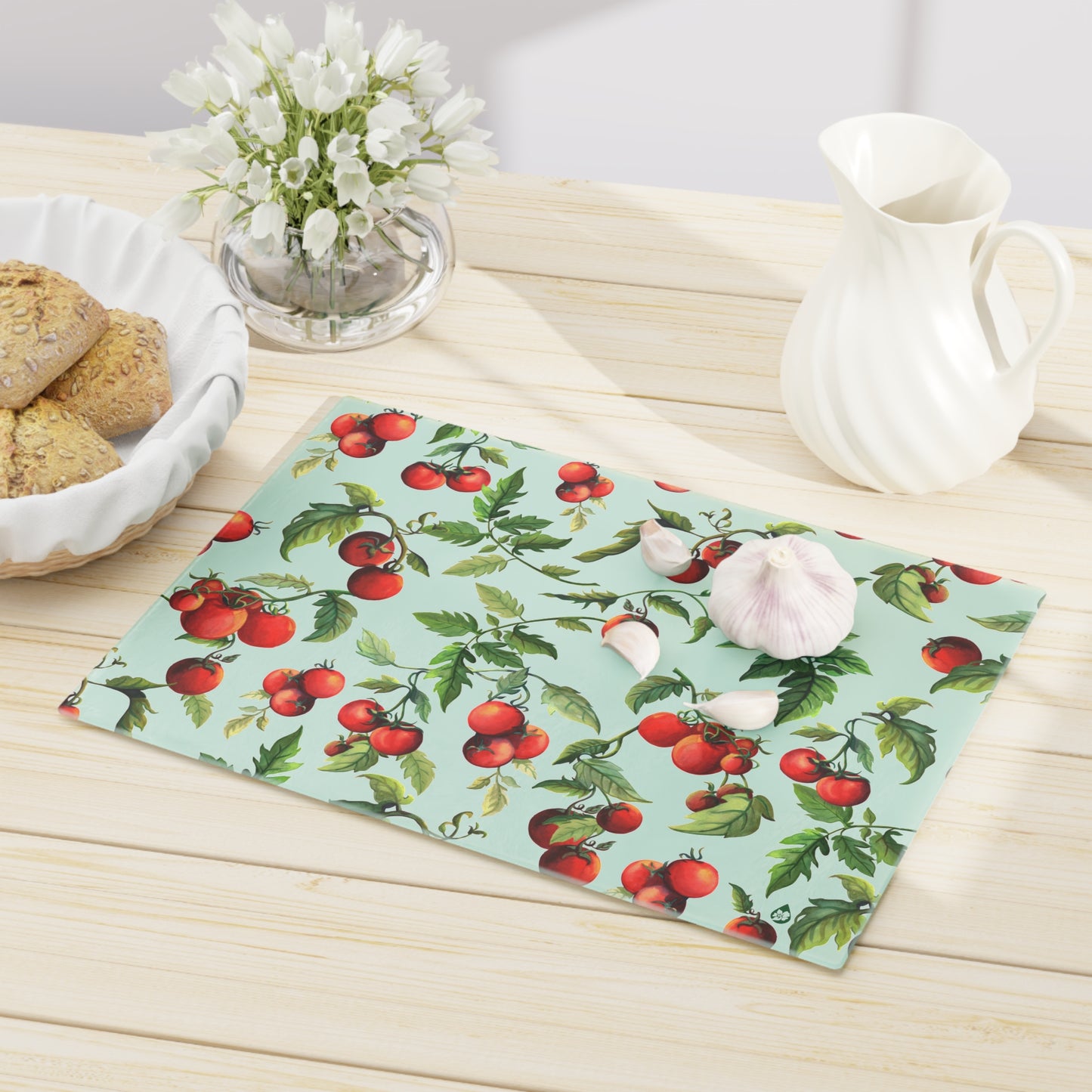 Tomato Tomato tempered glass cutting board on table with white pitcher vase of flowers and basket of bread