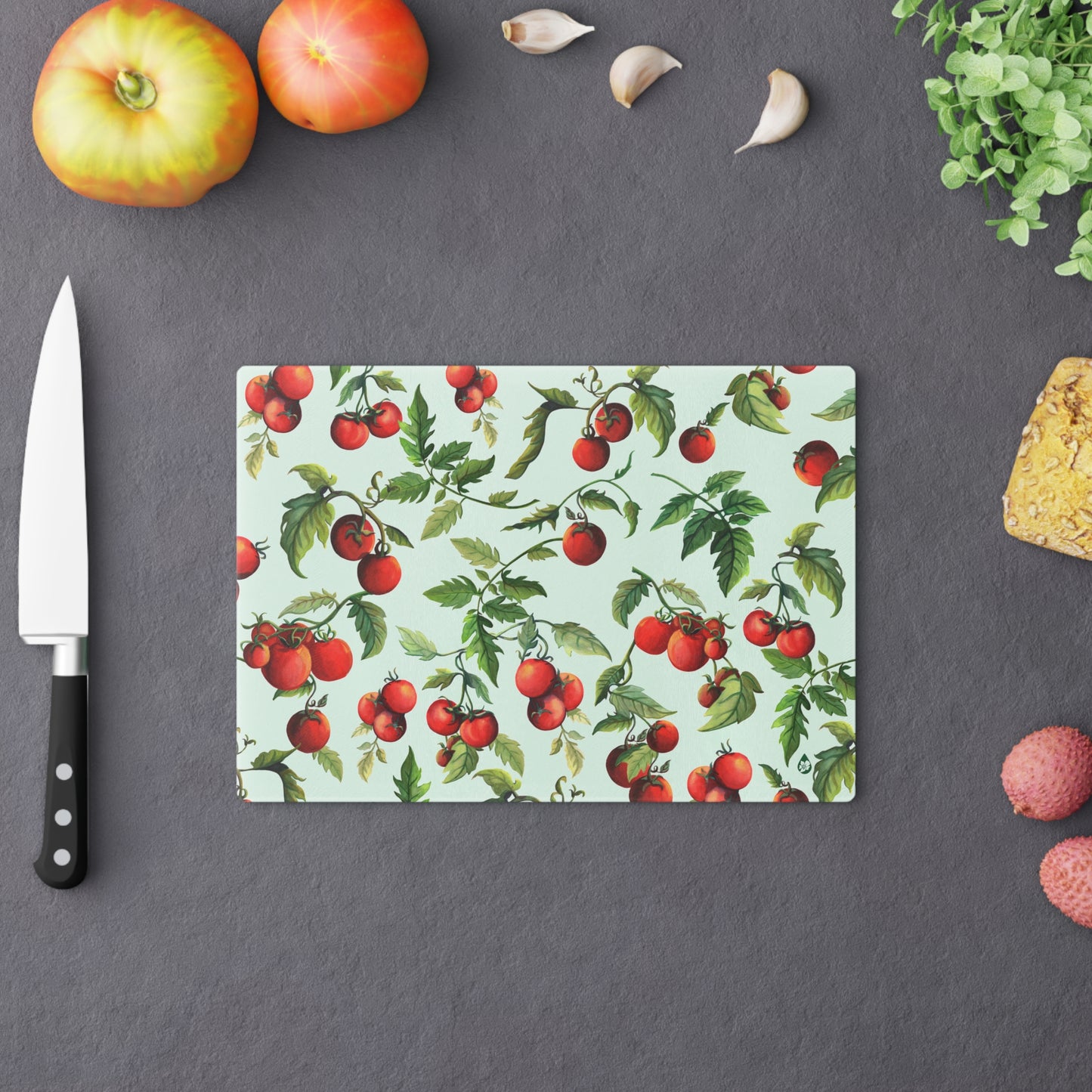 Small Tomato Tomato tempered glass cutting board on counter with fruit and chefs knife
