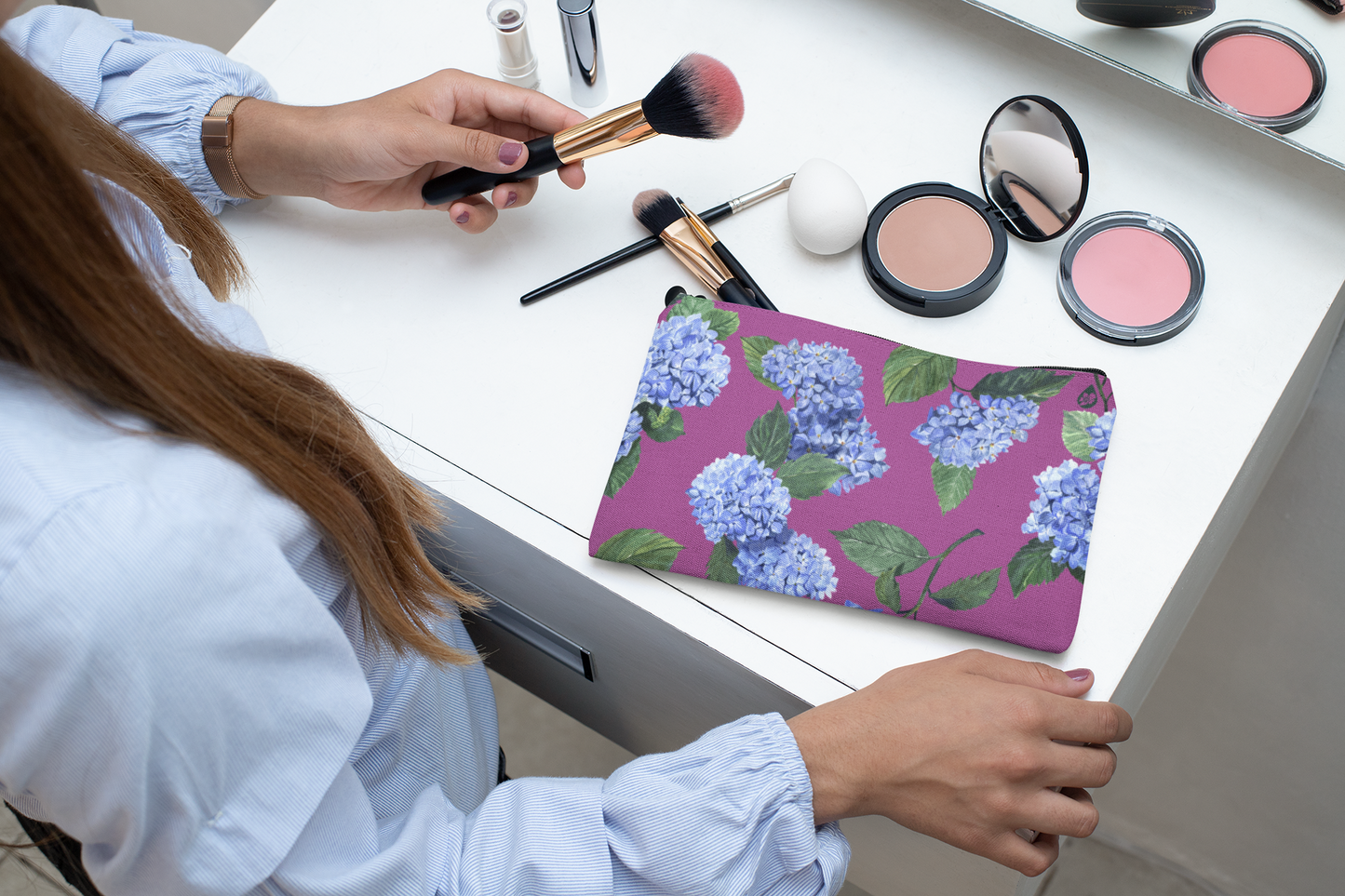 Woman putting on makeup from her Peony Pink Hydrangea Zip Pouch on vanity