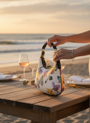 Arc and Air cream and floral Scoop bag held by woman on a beachfront table overlooking the ocean. 