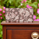 Floral-patterned wallet on a wooden surface with blurred pink flowers in the background