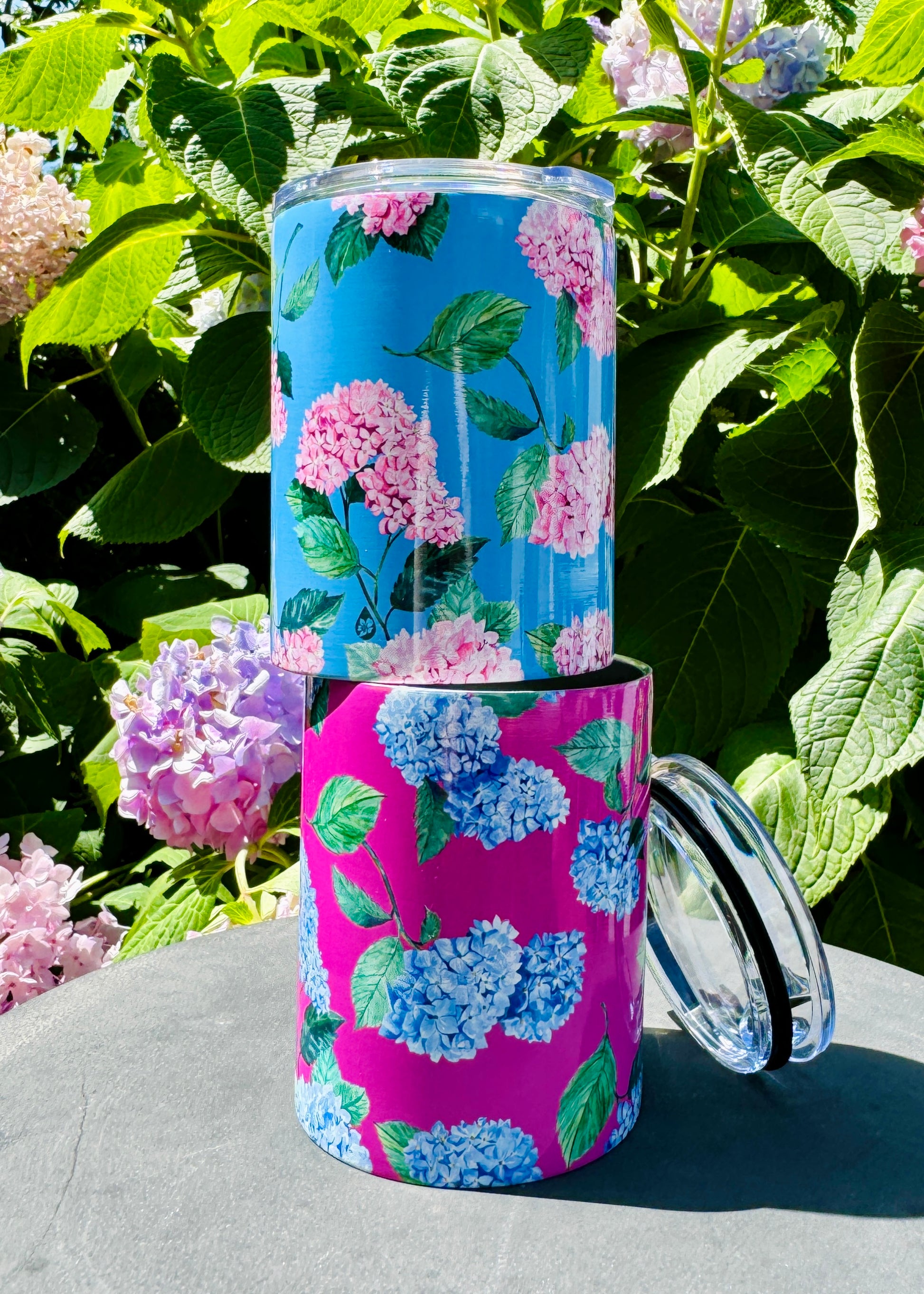 Hydrangea Tumbler Stacked on Garden Table in front of Hydrangea Shrub in Cloudless and Peony Pink