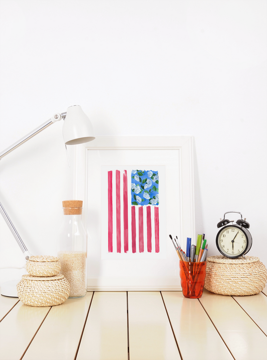Liberty print shown in white frame on desk with architect lamp and desk supplies