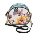An oval-shaped crossbody handbag with a colorful butterfly and orchid floral print on a light cream background, featuring a blue marbled top trim, a gold chain strap, and a black adjustable shoulder strap.