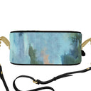 A round crossbody bag  view from the bottom, featuring an abstract ocean watercolor print in shades of blue, green, and beige, with a black leather strap and gold-tone chain links on a white background.