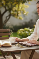 Woman sitting at a table outdoors with a cup of tea and an open book.
