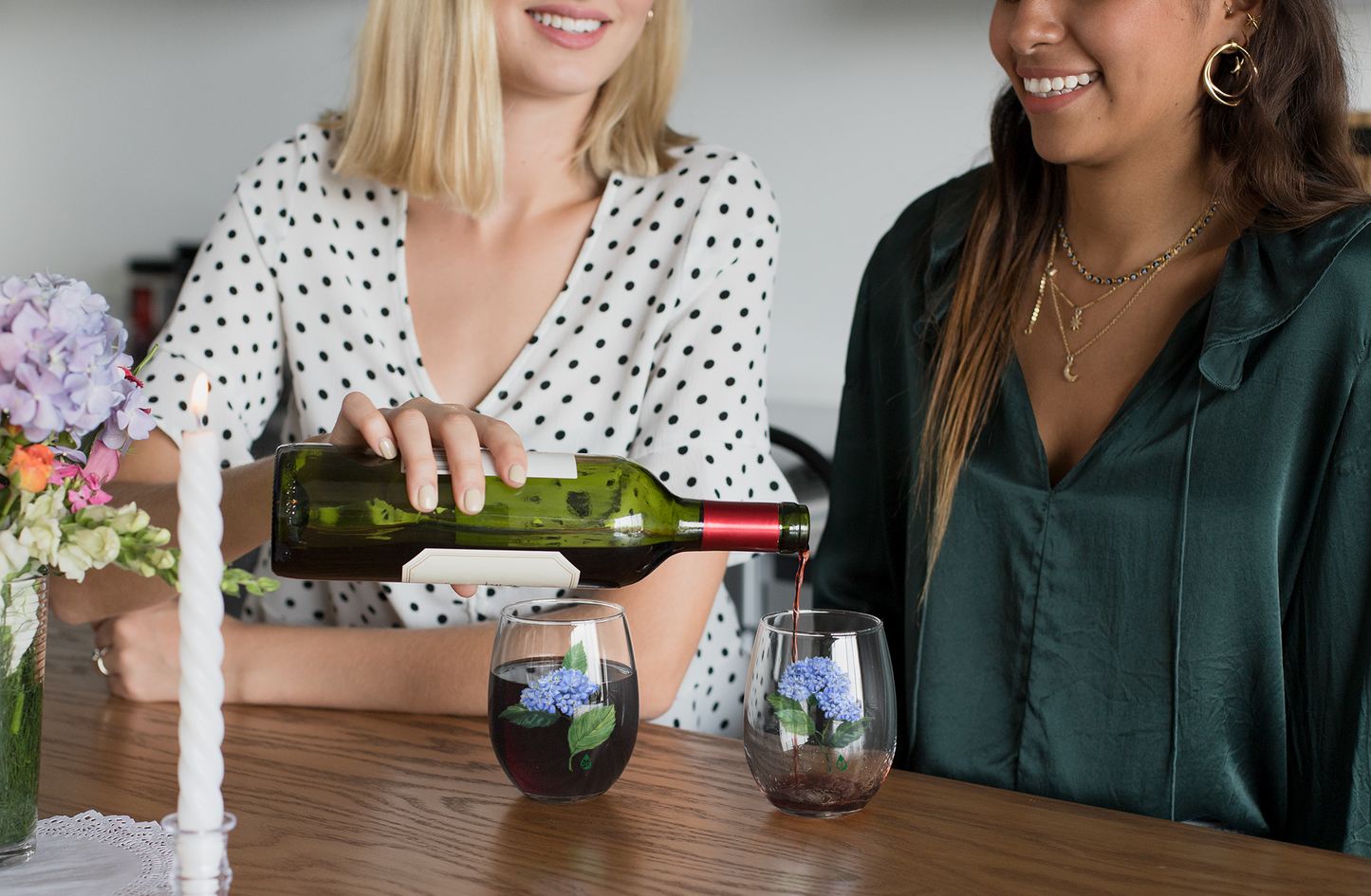 Two friends sharing a drink of red wine in stemless wine glasses with hydrangea paintings on them
