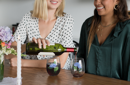 Two friends sharing a drink of red wine in stemless wine glasses with hydrangea paintings on them
